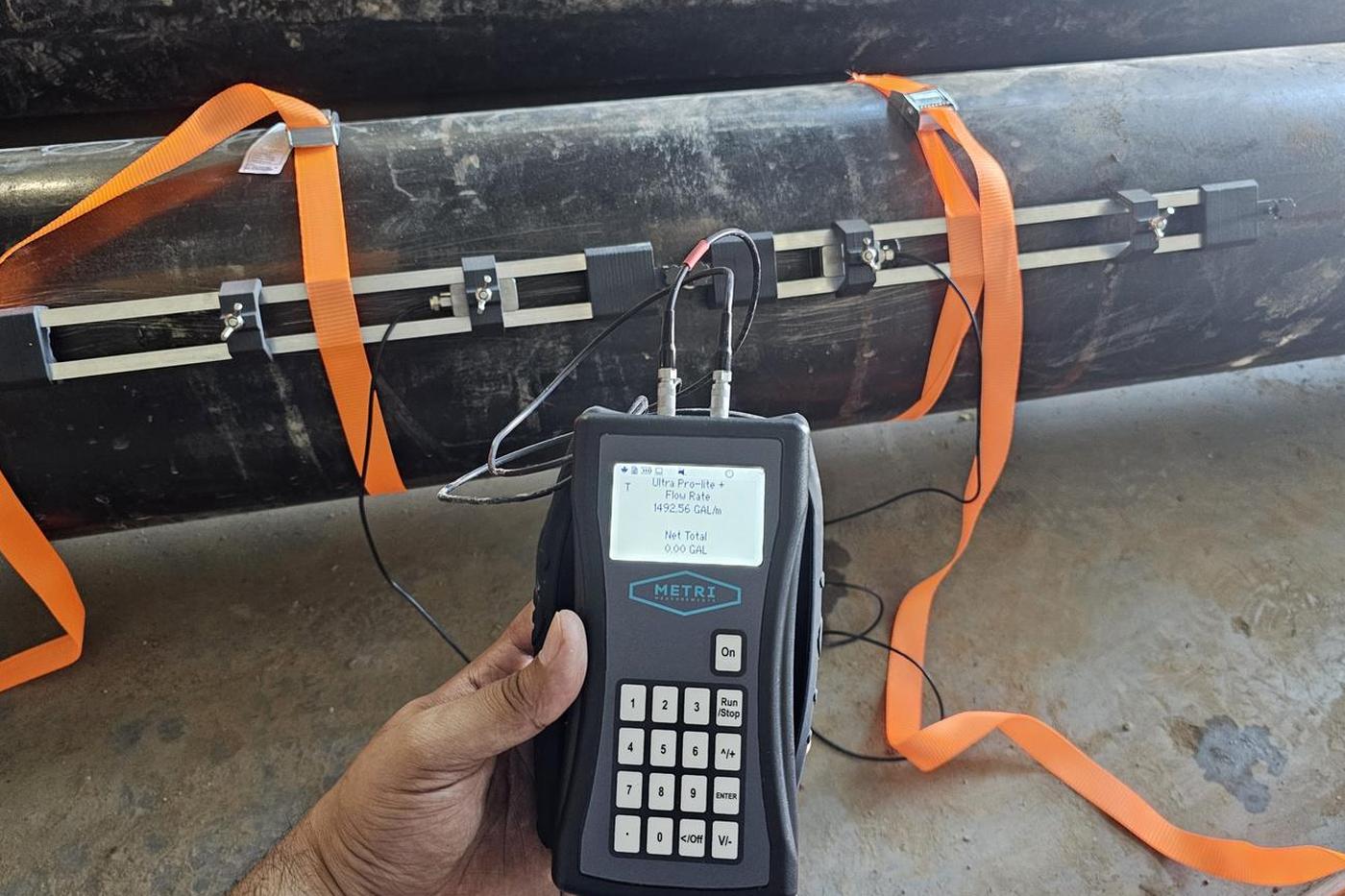 METRI Ultra Pro-lite portable clamp-on flow meter displaying a flow rate of 1,492.56 gallons per minute on a large-bore carbon steel pipeline