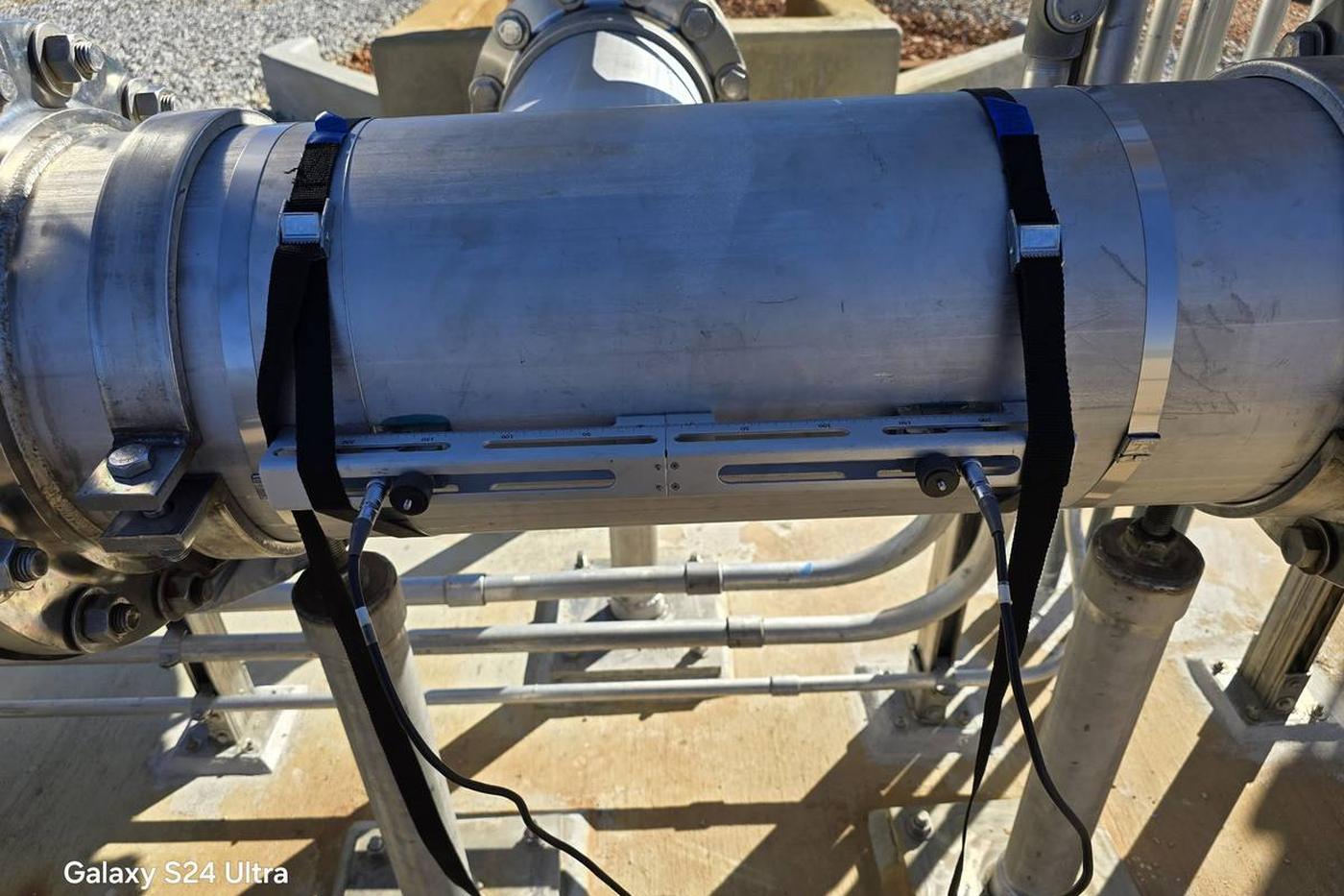 Clamp-on ultrasonic transducer rail strapped to a stainless steel process line on a skid