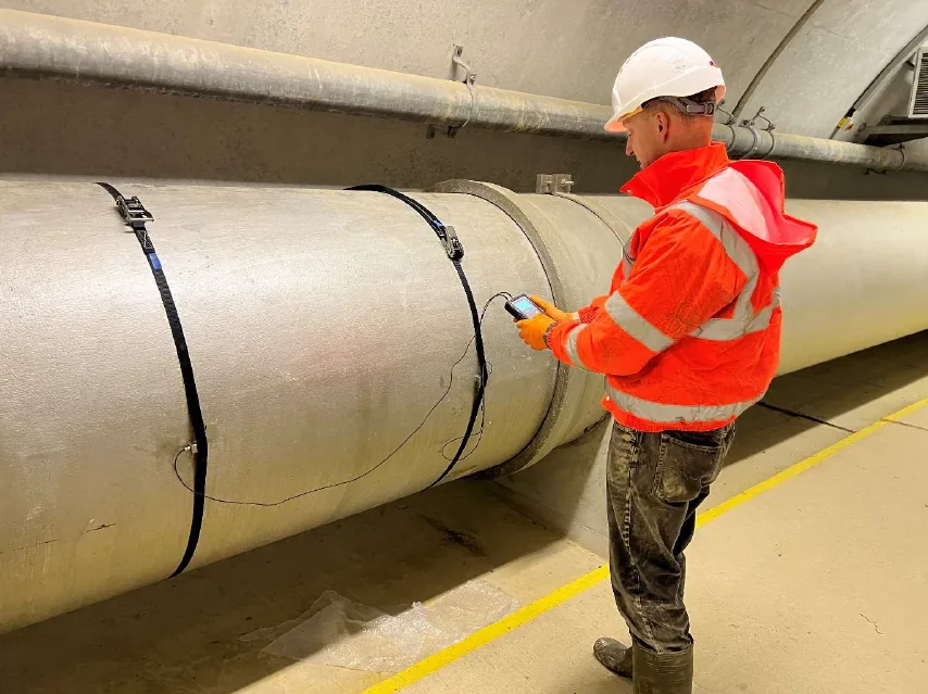 Technician surveying a large-bore pipe with a portable clamp-on flow meter